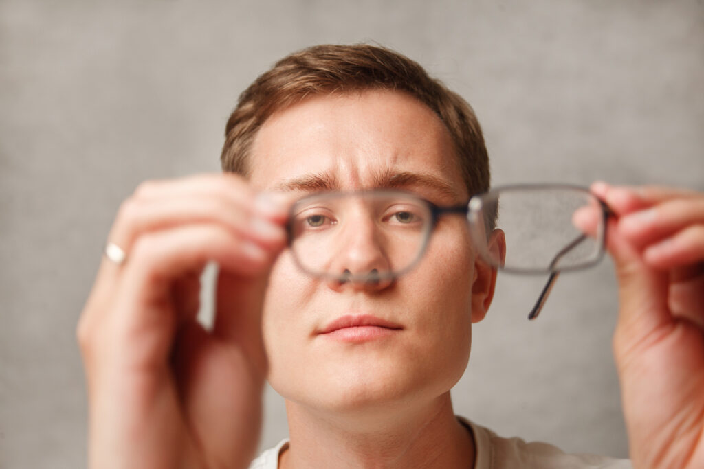 the young man holds glasses with diopter lenses and looks through them, the problem of myopia